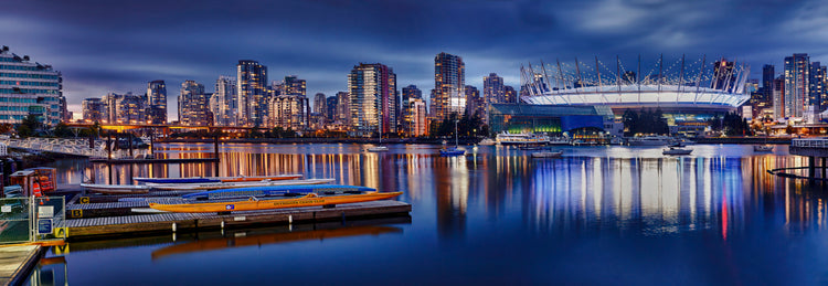 City skyline with modern architecture and a stadium at night, reflected in water.