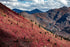 Mountain landscape with red and brown hues on a hillside under a cloudy sky.