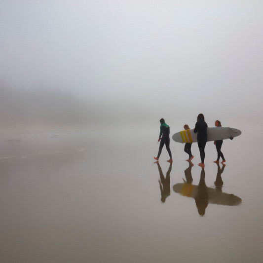 Three people with surfboards walking on a foggy beach